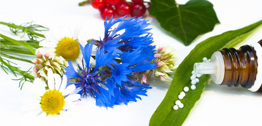 Symbolbild Naturheilkunde: Pflanzen, u.a. Mohn und kleine Kügelchen aus Medizinflasche