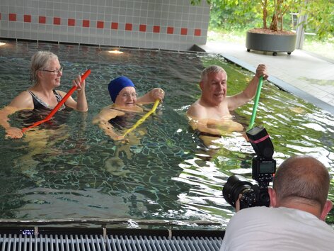 Making of Gruppe mit Sportgeräten im Schwimmbecken und Fotograf