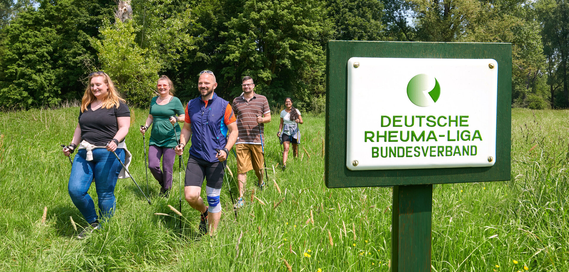 Gruppe von Menschen beim Nordic Walken, im Vordergrund Schild vom Deutschen Rheumaliga Bundesverband